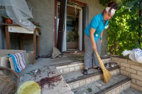 A local resident cleans up trash and fragments of a Russian bomb