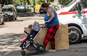 Жінка з дитячим візочком несе фанеру