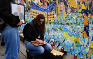 A woman decorates a frame with a portrait of a fallen soldier on Independence Square in Kyiv