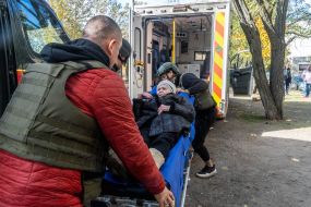 An elderly woman on a stretcher is carried into the cabin of an ambulance during an evacuation in the city of Kupyansk