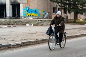 A woman rides a bicycle past destroyed houses in the village of Borovaya, Kharkiv region