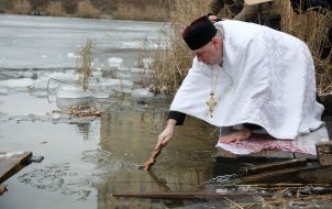 Священник освящает воду в Иорданском озере в Киеве