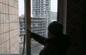 Женщина у разбитого окна смотрит на поврежденные дома после удара баллистикой по центральному району Киева