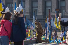 Молода людина стоїть навколішки біля прапорців на згадку про загиблих захисників України