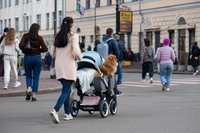 A woman carries a Spitz dog next to a child in a stroller