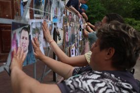 Женщины крепят на забор фотографии пропавших без вести