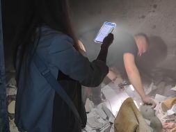 Чоловік та жінка при світлі мобільного телефона шукають кішку серед уламків в пошкодженій кімнаті гуртожитку НАУ в Києві