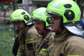 Спасатели сели отдохнуть на заборе возле жилого дома, в который попала ракета, в Соломенском районе в Киеве