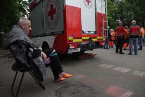 A man with a blanket on his shoulders sits on a chair in the yard near a residential building hit by a missile in the Solomianskyi district of Kyiv
