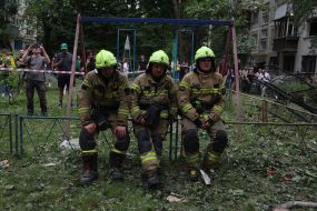 Спасатели сели отдохнуть на заборе возле жилого дома, в который попала ракета, в Соломенском районе в Киеве