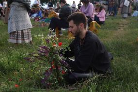 Участник празднования Ивана Купала собирает букет из полевых цветов
