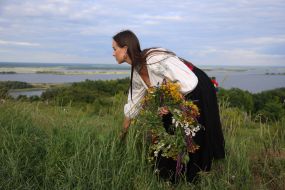 Участница празднования Ивана Купала собирает букет из полевых цветов