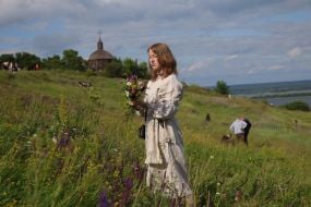 Участница празднования Ивана Купала собирает букет из полевых цветов