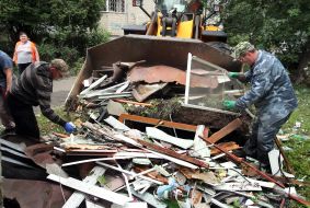 Utility workers near a house damaged by shelling