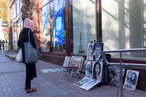 A woman looks at portraits painted by a street artist on a street in central Kyiv
