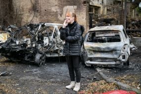 Женщина курит возле сгоревших автомобилей