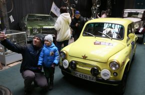 A man takes a selfie with a boy in front of a retro car