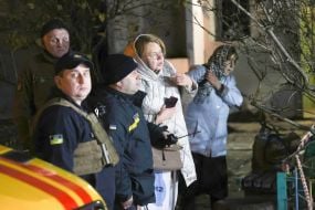 Люди стоять на вулиці біля пошкодженого після нічної атаки російської федерації житлового будинку  в Оболонському районі міста Києва