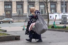 An elderly woman carries things in a large scarf on the street in Kyiv