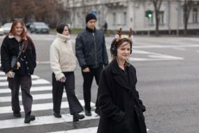 A girl wearing a hoop with deer antlers crosses the street in Kyiv