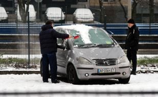 Мужчина чистит лобовое стекло автомобиля от снега на улице в Киеве