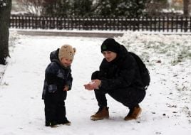 Мужчина показывает ребенку снег в руках на улице в Киеве