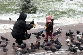 A woman takes a photo of a child on a snowy street in Kyiv