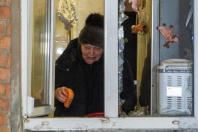 Woman cleaning up broken glass in an apartment damaged by Russian shelling