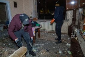 People cleaning up broken glass in an apartment damaged by Russian shelling