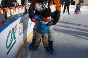 Маленький хлопчик за допомогу дорослого катається на ковзанах  на ковзанці на Контрактовій площі в Києві