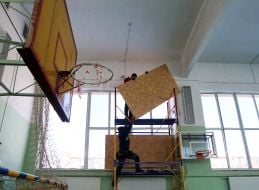 Covering up broken windows in a school gym with plywood after Russian shelling
