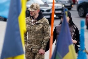 Военнослужащий с маленькой собачкой за пазухой у флажков в память о погибших защитниках Украины