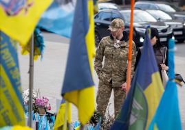 Военнослужащий с маленькой собачкой за пазухой у флажков в память о погибших защитниках Украины