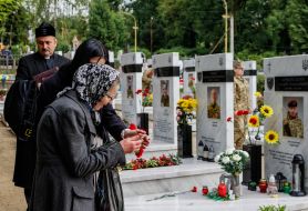 Женщины и священник возле могил погибших защитников Украины