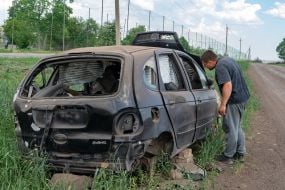 Мужчина осматривает сожженный автомобиль на обочине дороги в Харьковской области