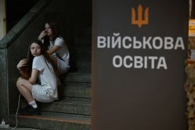 Girls sit on the stairs near the sign "Military Education"