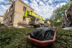 Тело погибшего на фоне полуразрушенного в результате российской атаки дома
