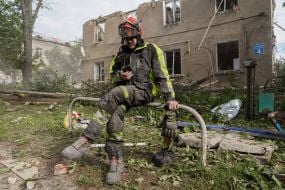 Спасатель  на фоне полуразрушенного от российской атаки жилого дома