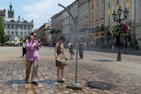 Люди охолоджуються біля вуличних розпилювачів води під час сильної літньої спеки у Львові