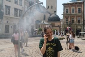 People cool off near street water sprinklers during the intense summer heat in Lviv