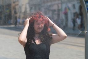 People cool off near street water sprinklers during the intense summer heat in Lviv