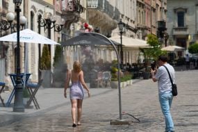 People cool off near street water sprinklers during the intense summer heat in Lviv