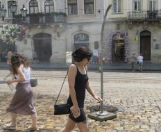 People cool off near street water sprinklers during the intense summer heat in Lviv