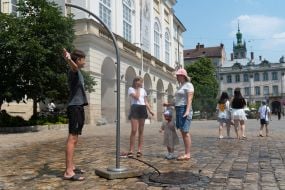 People cool off near street water sprinklers during the intense summer heat in Lviv