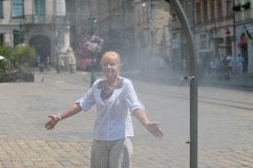 People cool off near street water sprinklers during the intense summer heat in Lviv