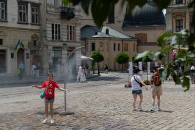People cool off near street water sprinklers during the intense summer heat in Lviv