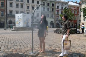 People cool off near street water sprinklers during the intense summer heat in Lviv