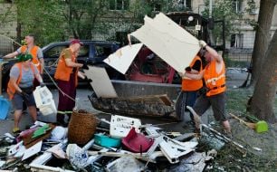 Співробітники комунальної служби прибирають біля будинку, постраждалого внаслідок масованого російського обстрілу