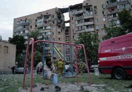 A woman on a swing near a high-rise building partially destroyed as a result of the delivery of a Russian missile in the Podilskyi district of Kyiv