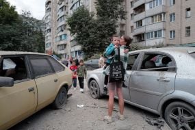 Woman with child in arms near damaged cars at one of the locations after the massive attack on Kyiv